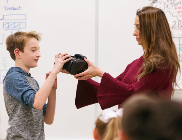 A boy taking VR goggles from a female teacher.