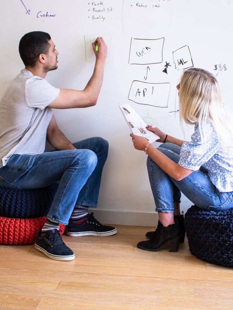 Two people sitting on cushions drawing diagrams on a whiteboard.