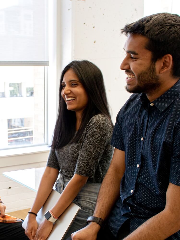 Three people seated at a desk, talking and laughing.